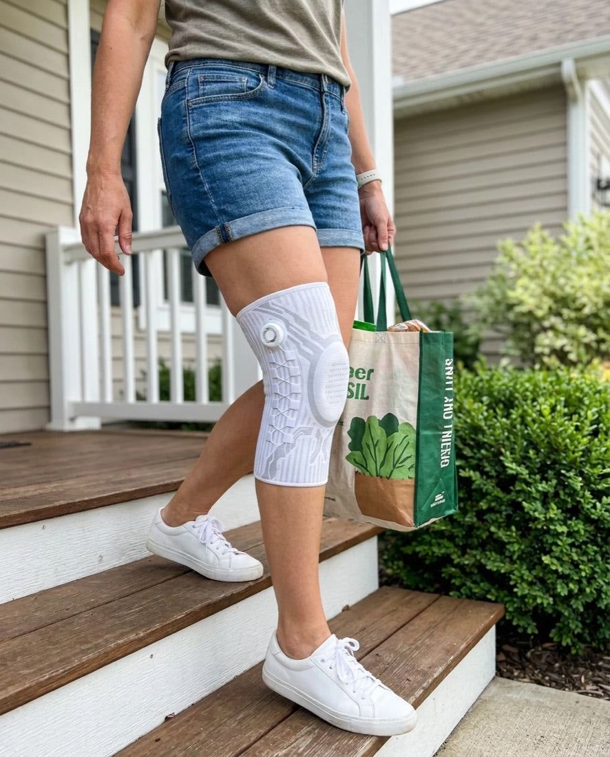 Woman stepping down porch steps with groceries wearing a white Chipaki knee brace